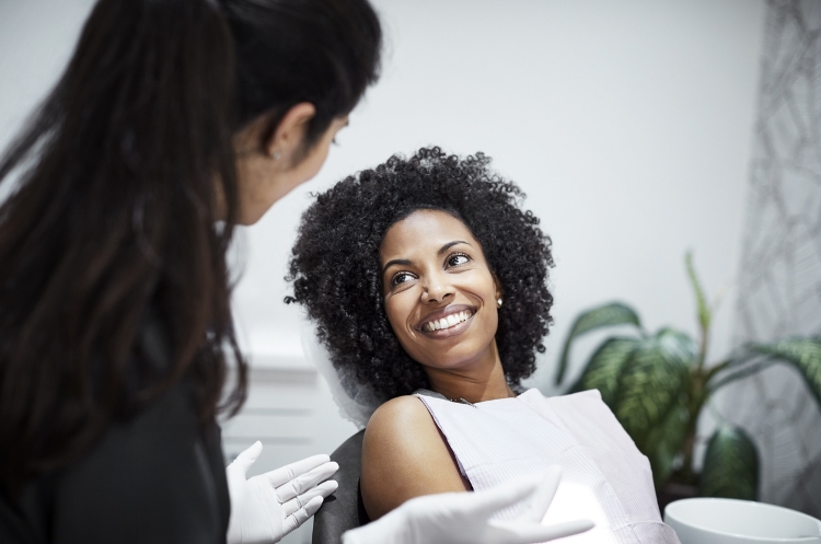 Smiling woman with curly hair at a dental clinic, interacting with a friendly dentist or healthcare professional during a checkup, in a modern medical office setting.
